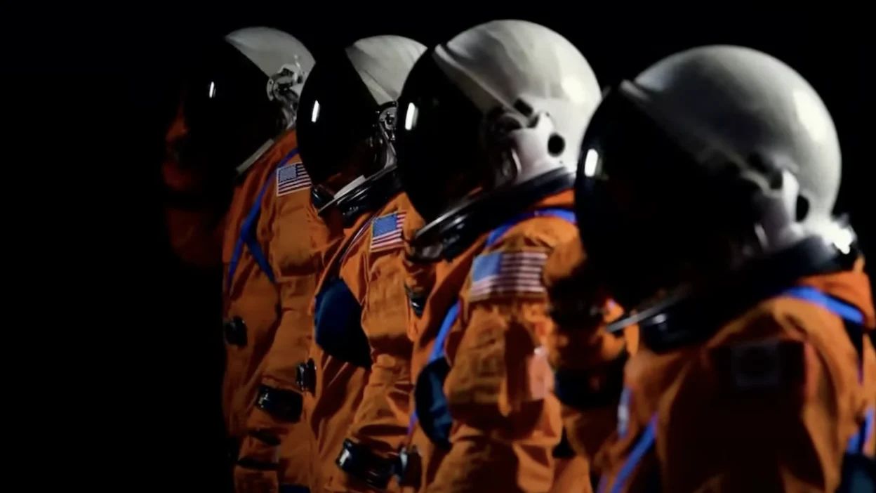 four spacesuits stand with white helmets.