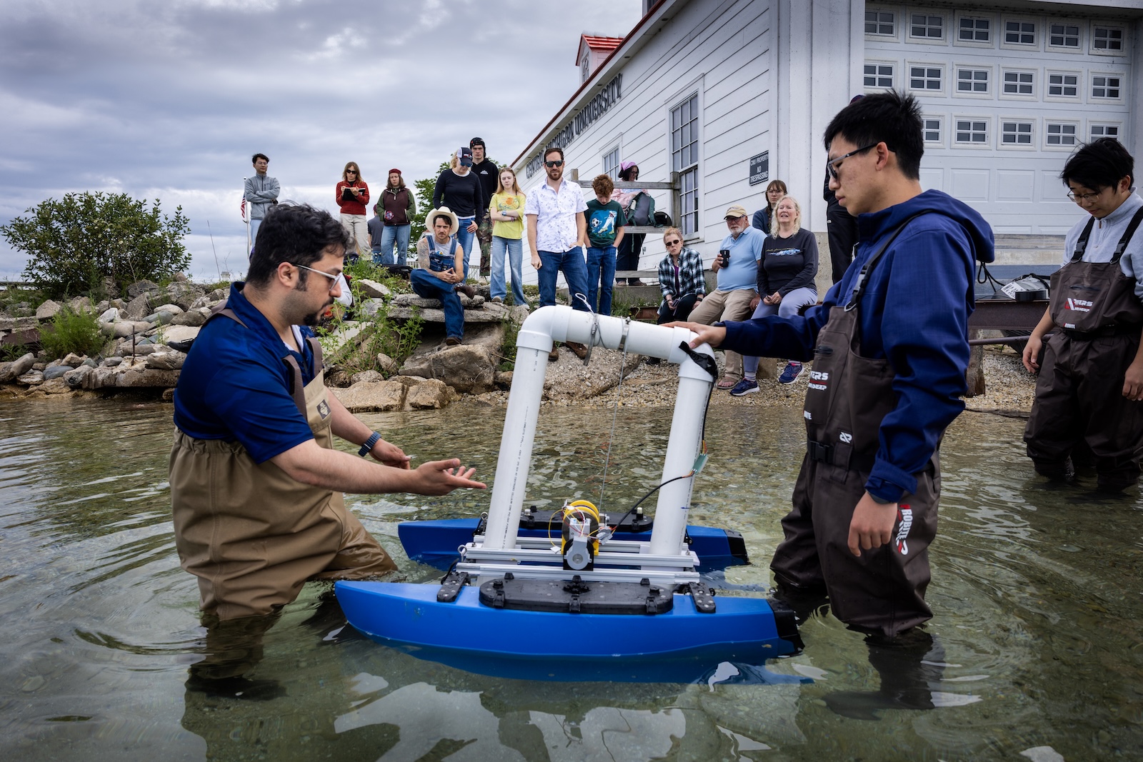 Team members presenting a floating wave-energy device to a group gathered along the waterfront.