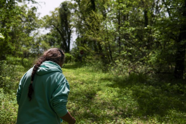 Cathi Murray walks on the overgrown dirt road behind her home as she looks for sparkling bits of coal ash on the dirt in Town of Pines, Indiana, on May 21, 2026. (Eileen T. Meslar/Chicago Tribune)