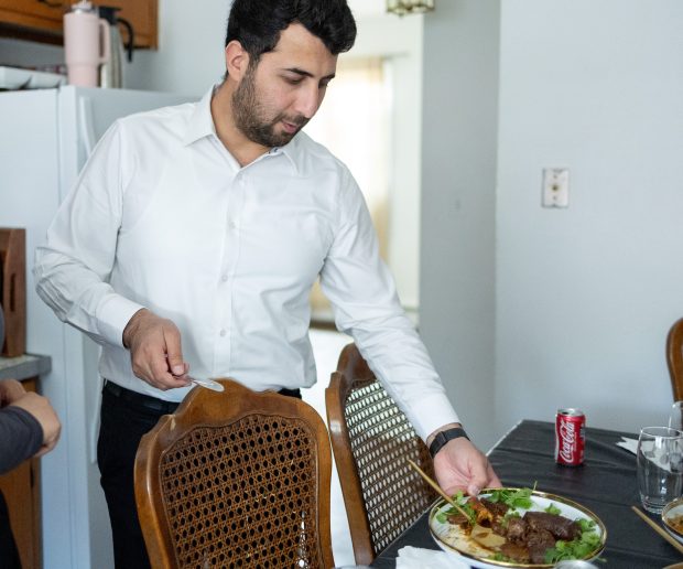 Abdulhaq Sodais speaks with his wife as he picks up a plate of food after eating lunch at their home in Evanston on May 8, 2026. Sodais is an Afghan refugee who immigrated to the United States in December of 2025. (Josh Boland/Chicago Tribune)