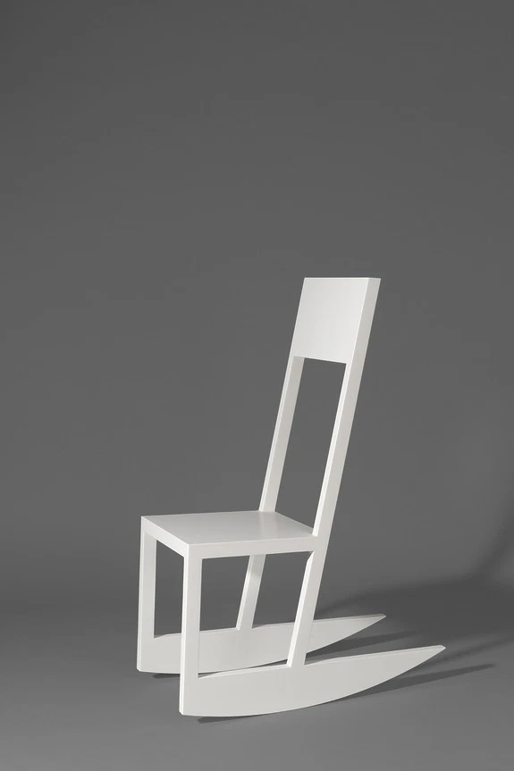 Modern white minimalist chair on a gray background with angled lighting and strong shadow.