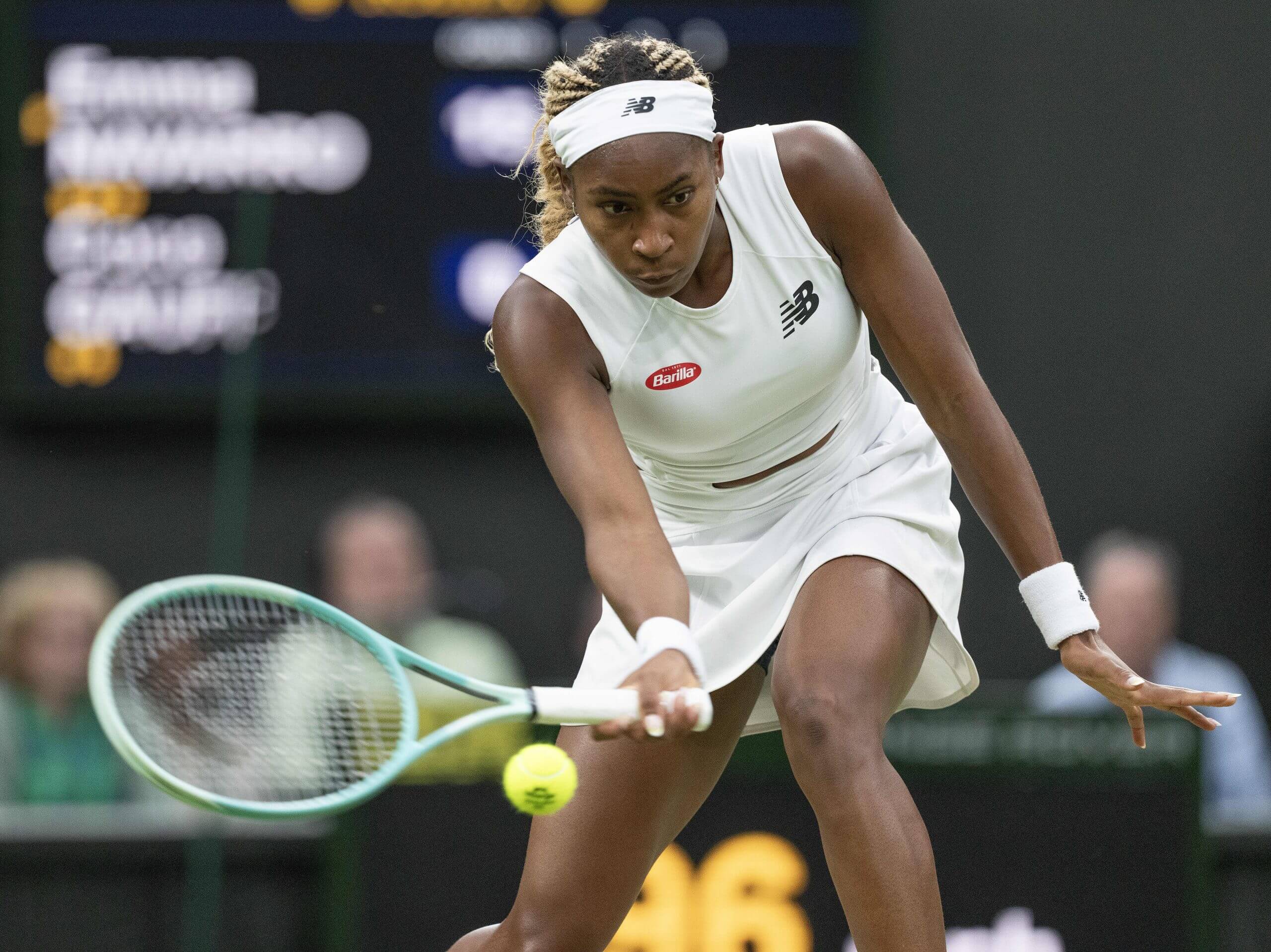Coco Gauff hits a forehand slice low to the ground wearing all-white tennis gear.