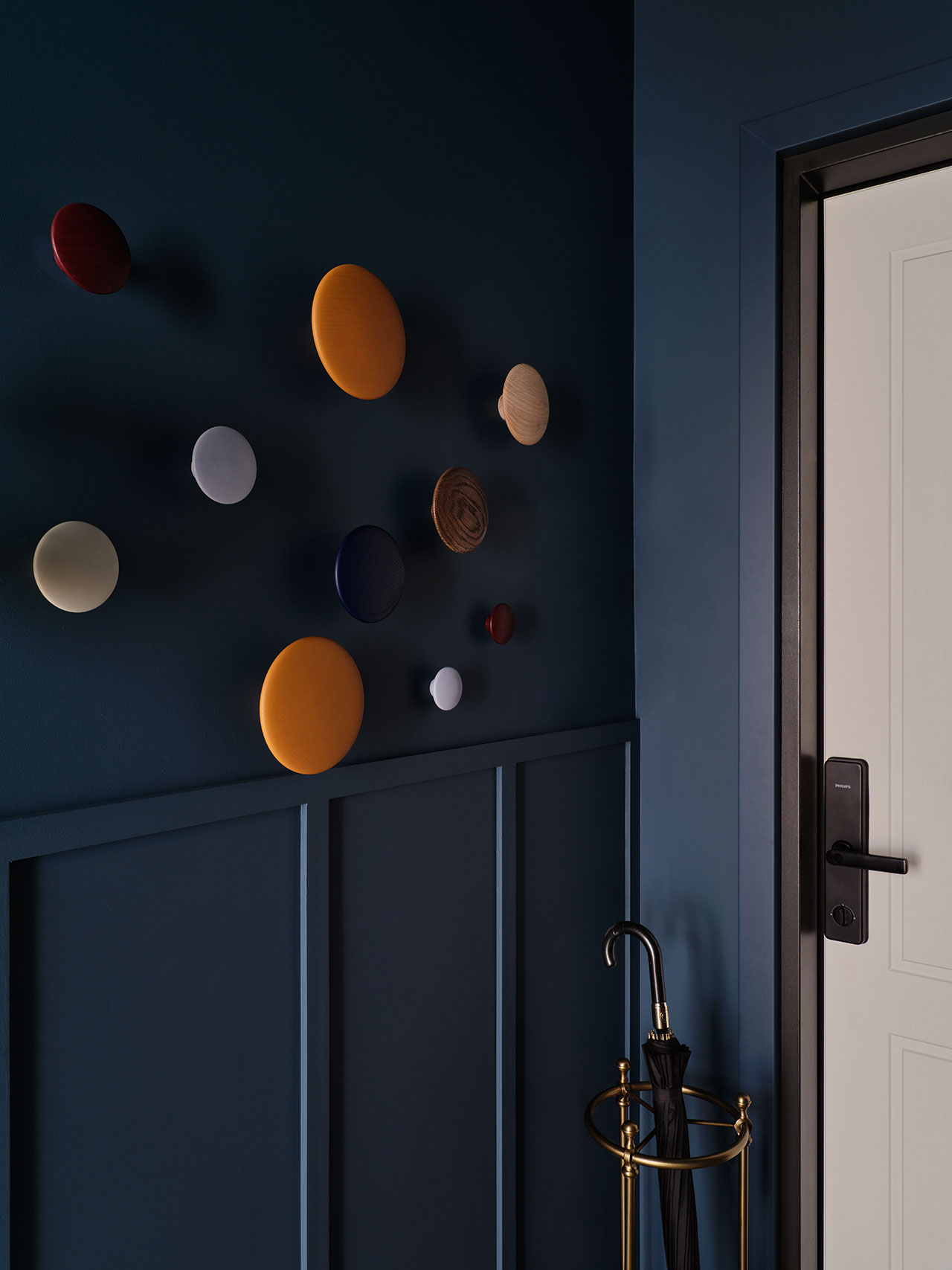 A dark blue entryway features round, multicolored wall hooks next to a white door and an umbrella in a gold stand.