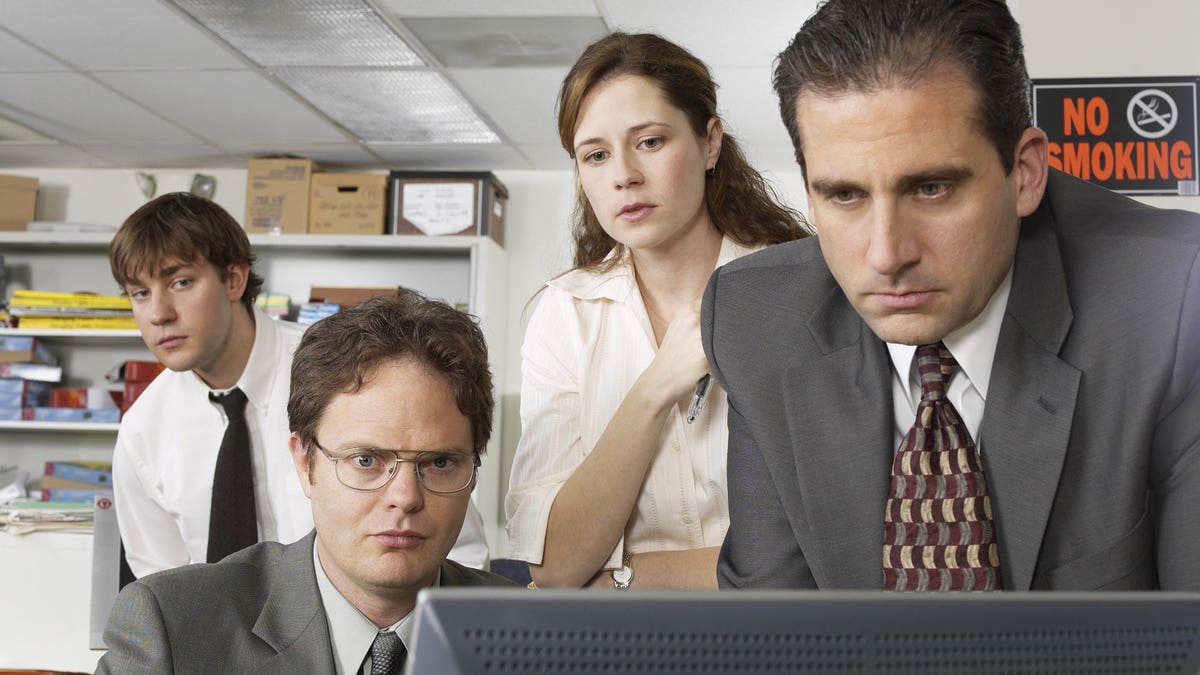 John Krasinski as Jim Halpert, Rainn Wilson as Dwight Schrute, Jenna Fischer as Pam Beesly, and Steve Carell as Michael Scott standing in an office setting