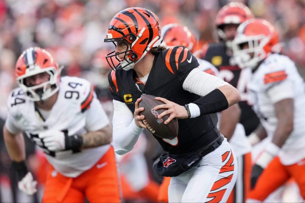 Bengals quarterback Joe Burrow runs during game action with two hands on the football while being chased by members of the Browns.