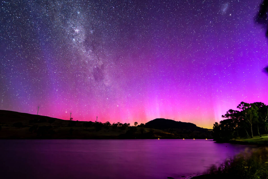Aurora Australis illuminates the night sky in shades of purple and pink above a calm lake in regional NSW