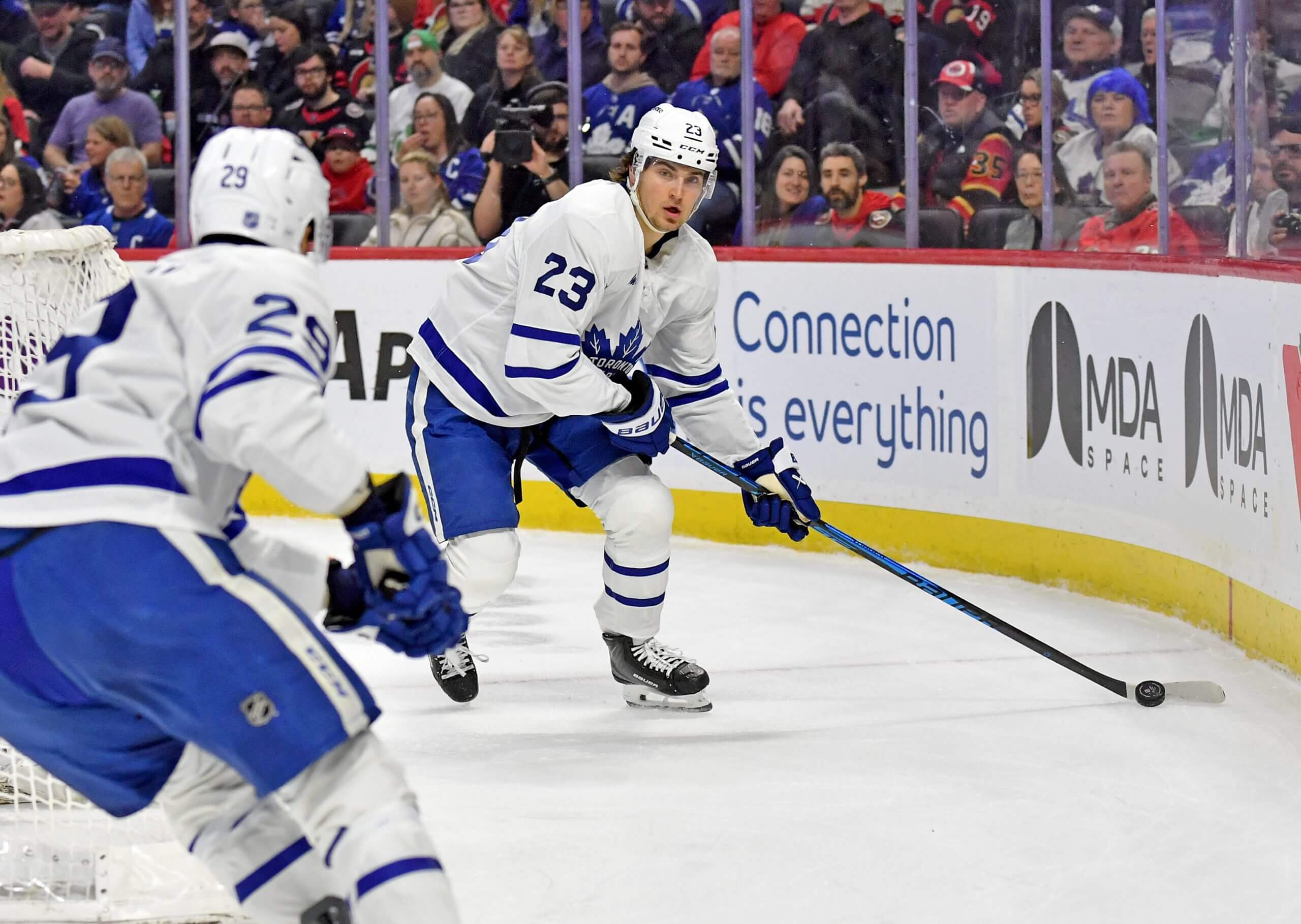 Matthew Knies makes a pass near the boards during a Leafs game, with a teammate skating into the frame.