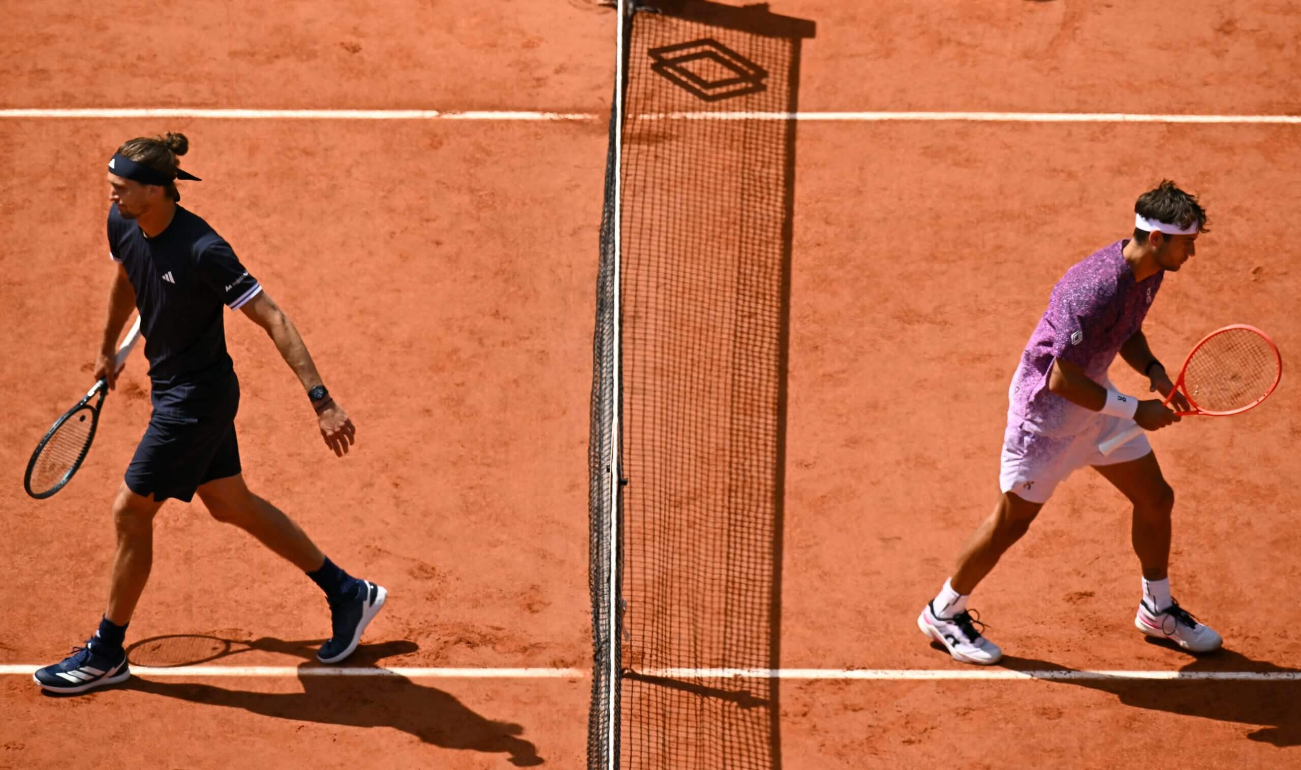 Alexander Zverev and Flavio Cobolli walk away from each other on a clay tennis court.