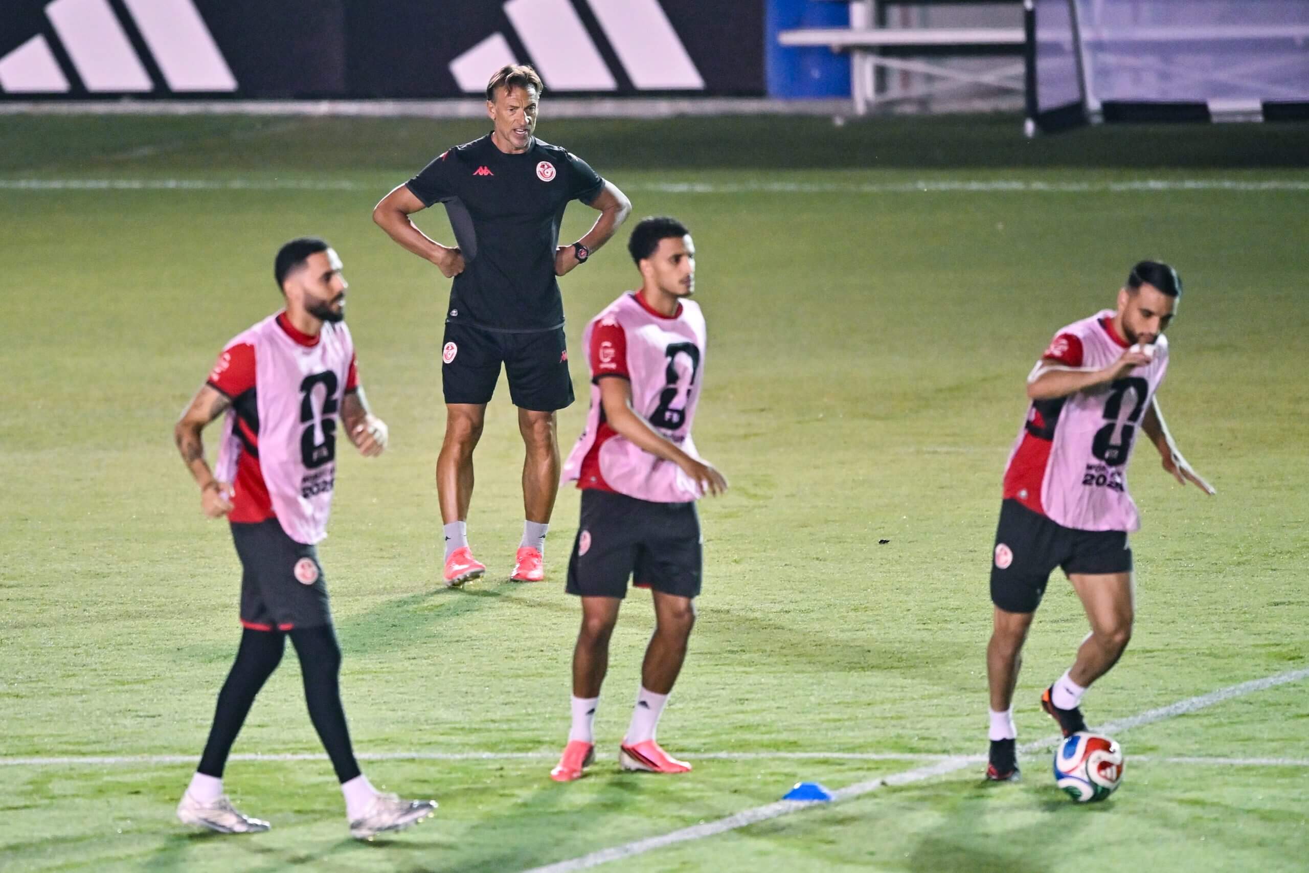 A football coach stands on a pitch as his players train