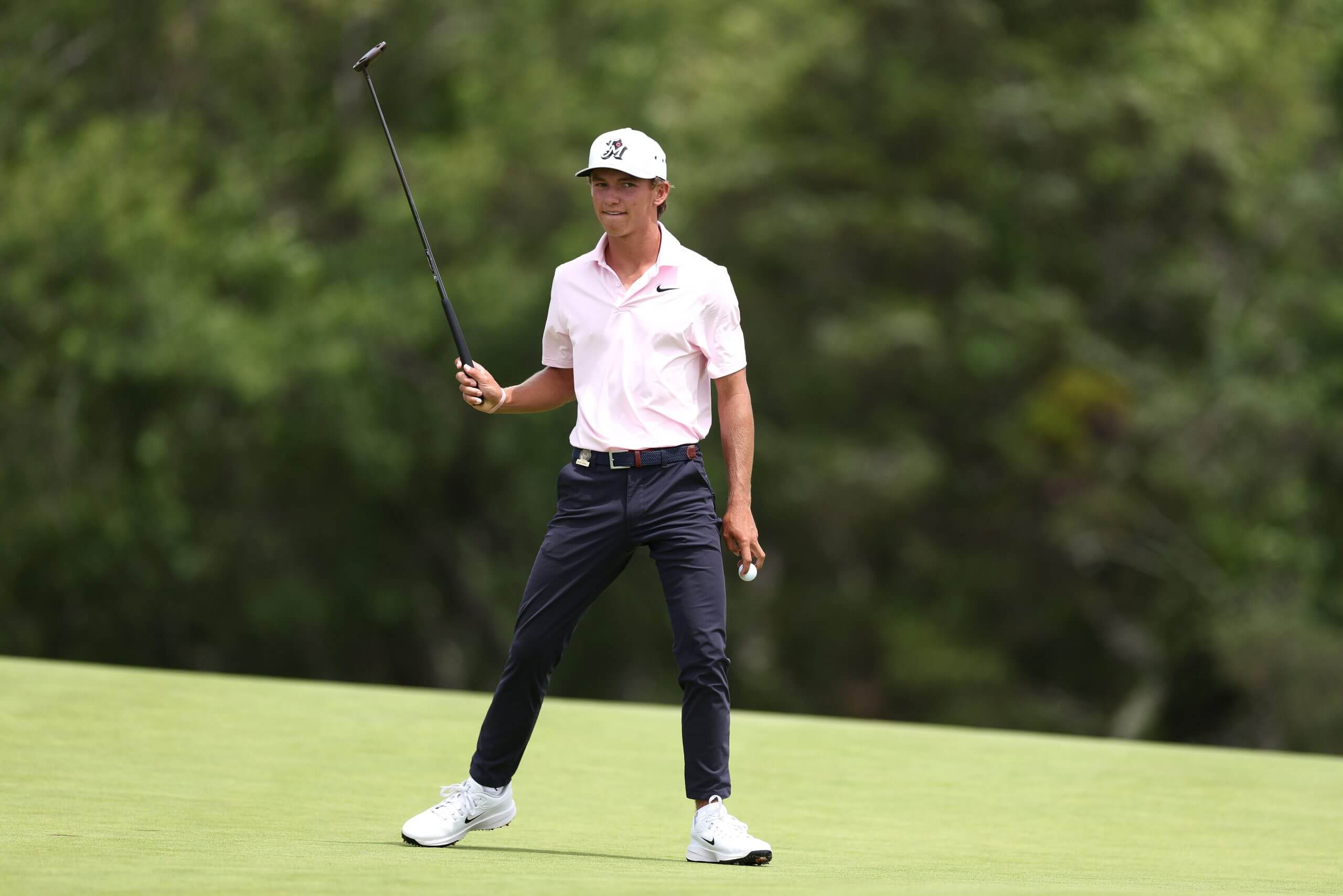 Miles Russell holds his ball between the first two fingers of his left hand and raises his putter perpendicular to the ground with his right hand.