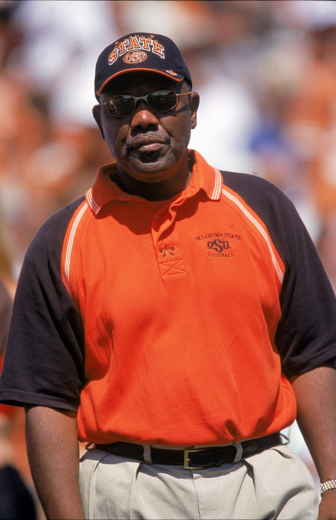Bob Simmons, former football coach for Oklahoma State, in a black and orange OSU polo shirt and an OSU cap, wearing sunglasses.
