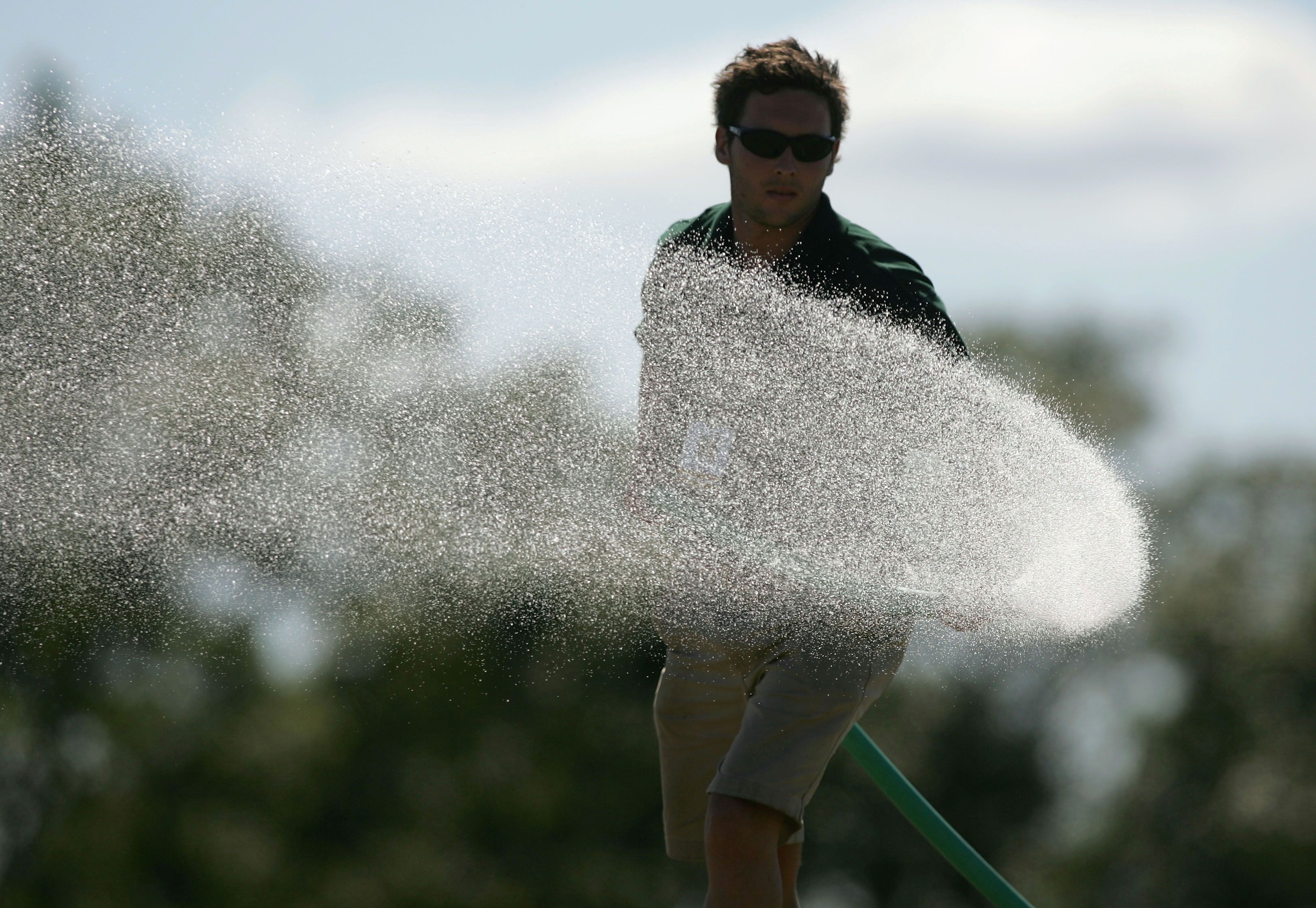 Large spray of water from a hose, with a person watering in the background.