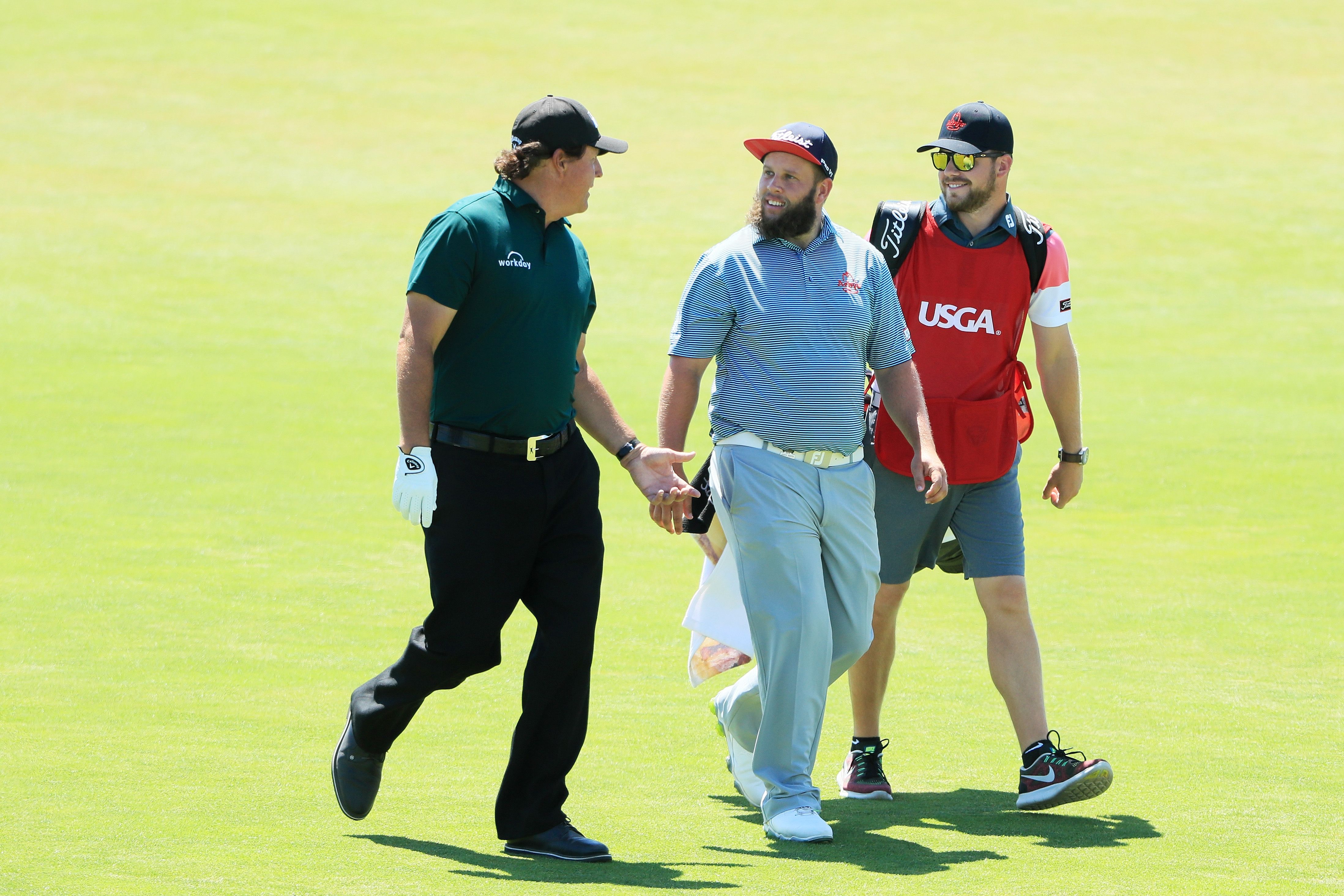 Two golfers and their caddie walk together on a sunny green golf course.