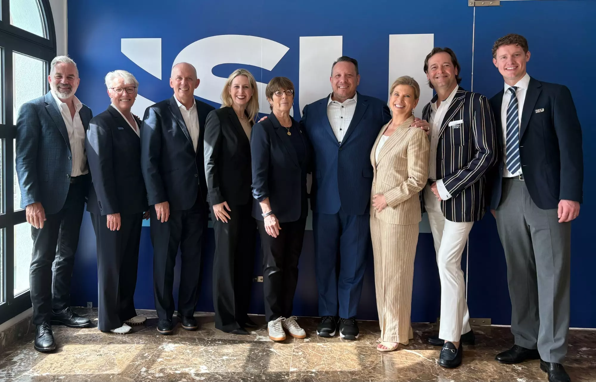 A U.S. Figure Skating delegation stands in front of the ISU Congress banner. (l-r) Kevin Rosenstein, Lois Long, Pat St. Peter, Troy Goldstein, Matt Farrell, Karin Sherr, Tina Lundgren, Shawn Rettstatt and Evan Bates