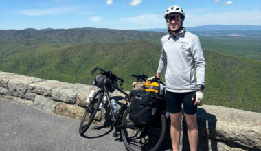 Tim Milich standing next to his bike posing for a photo in front of a green landscape behind him.