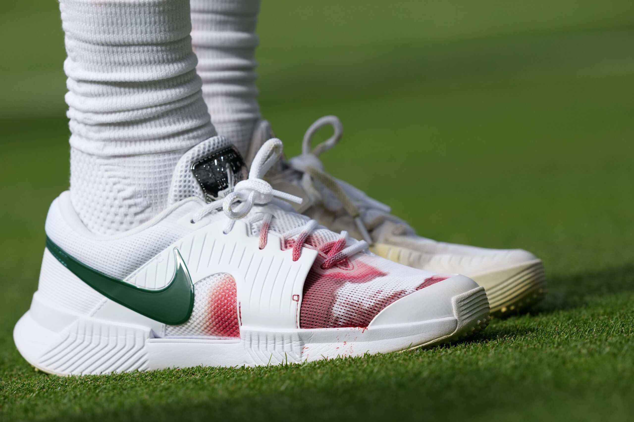 A tennis shoe with green tick and red for the Italian flag gets more red at the front thanks to blood coming from a player's foot.