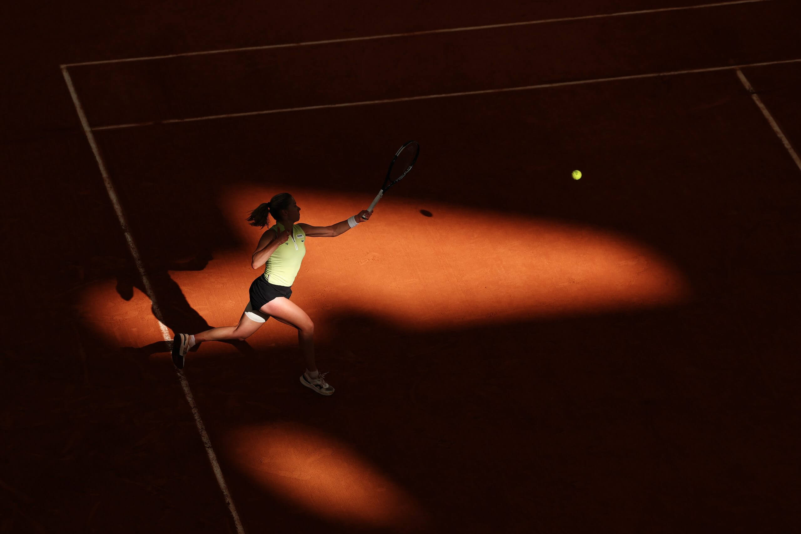 Maja Chwalińska hits a left-handed forehand on a clay court dappled with sun.