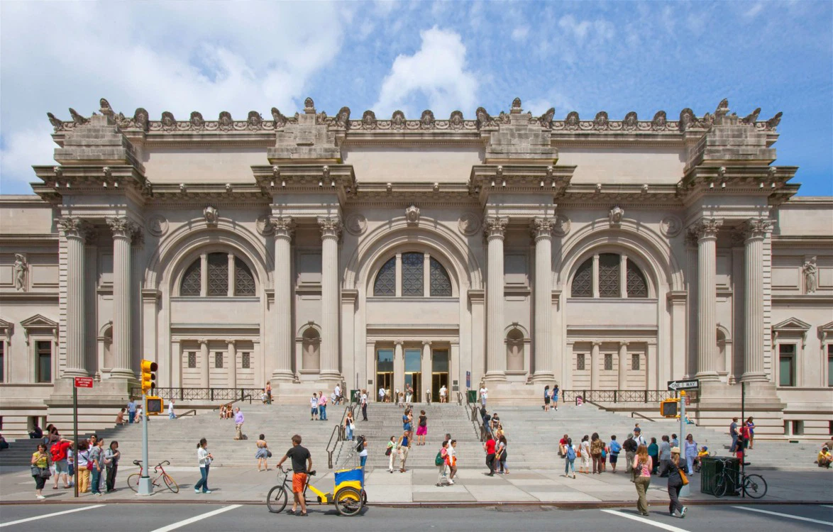 Exterior view of a the Metropolitan Museum of Art with a grand entrance and ornate architectural details, people walking in front.