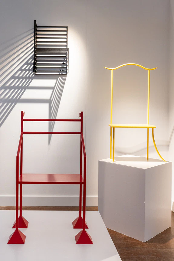 Red and yellow modern art sculptures displayed in a gallery setting with shadows cast on a white wall.