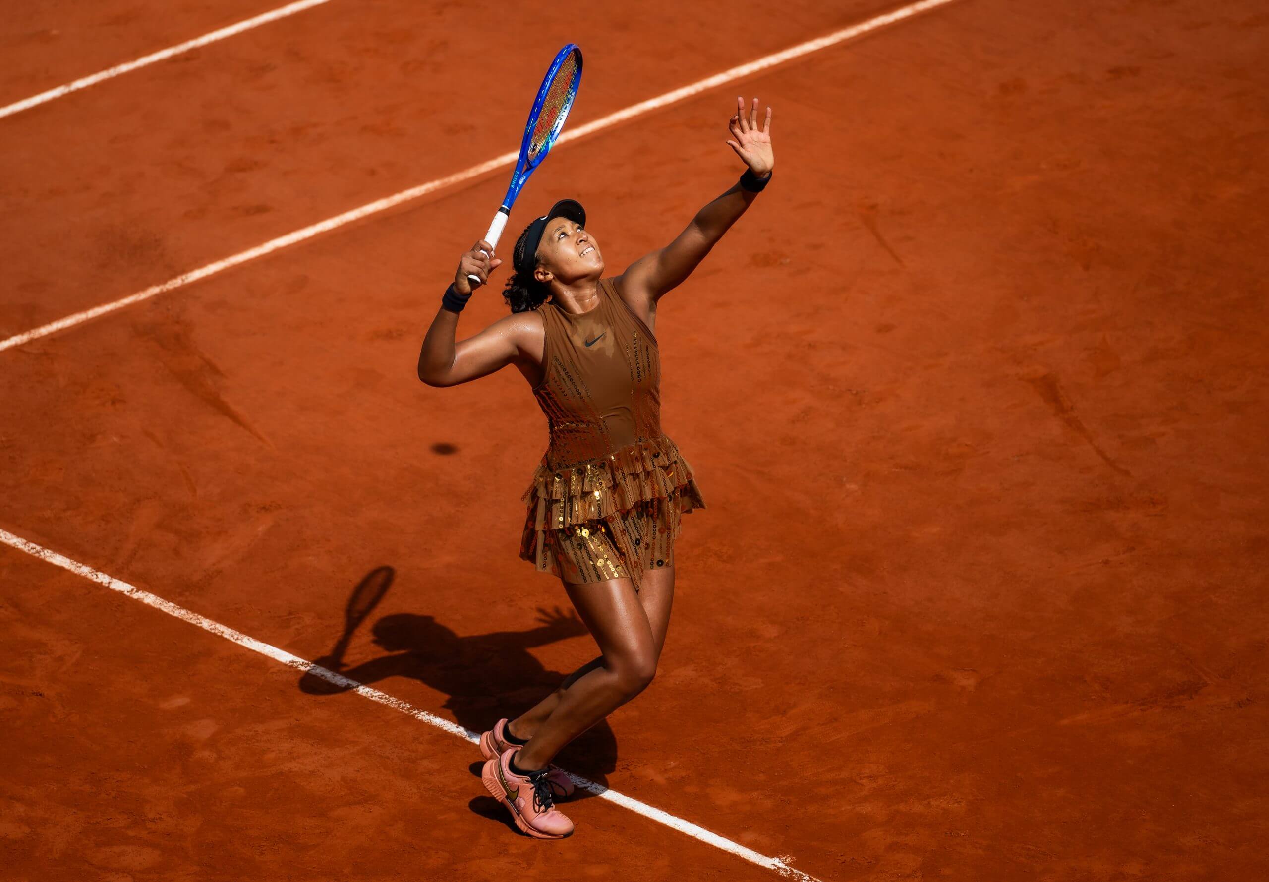 Naomi Osaka hits a serve on a clay tennis court