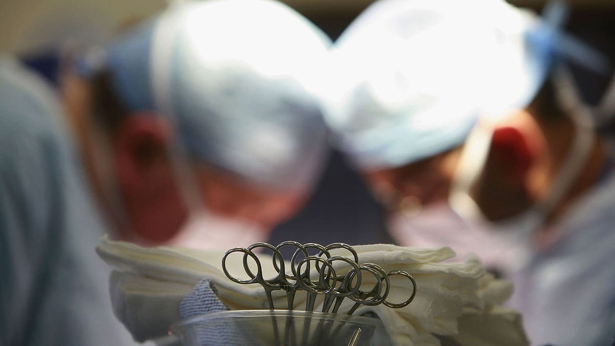Medical staff perform a procedure in an operating room with surgical instruments visible in the foreground.