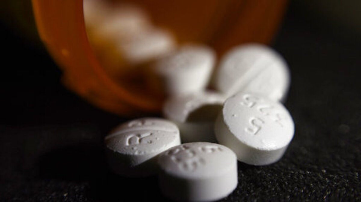 Opioid medications are shown coming outside a prescription bottle. Opioid medications are shown coming outside a prescription bottle.
