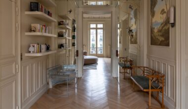 A grand hallway with off-white walls, paneling, and open shelving with seating benches along either side of the walls and paintings along the right-hand side