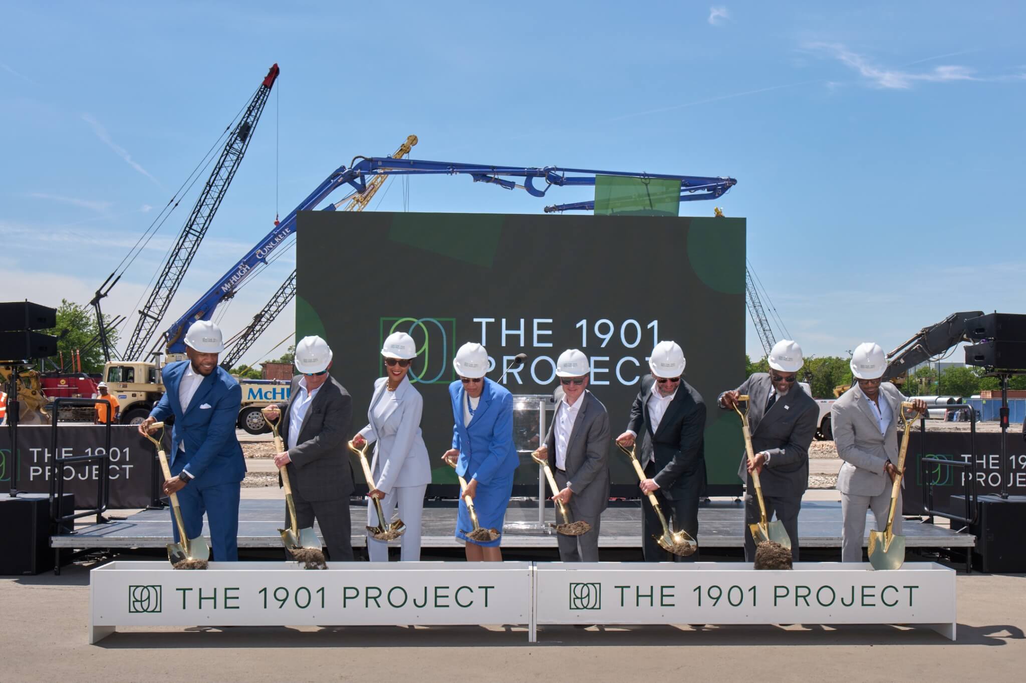 Eight people in hard hats hold gold shovels at the 1901 Project groundbreaking