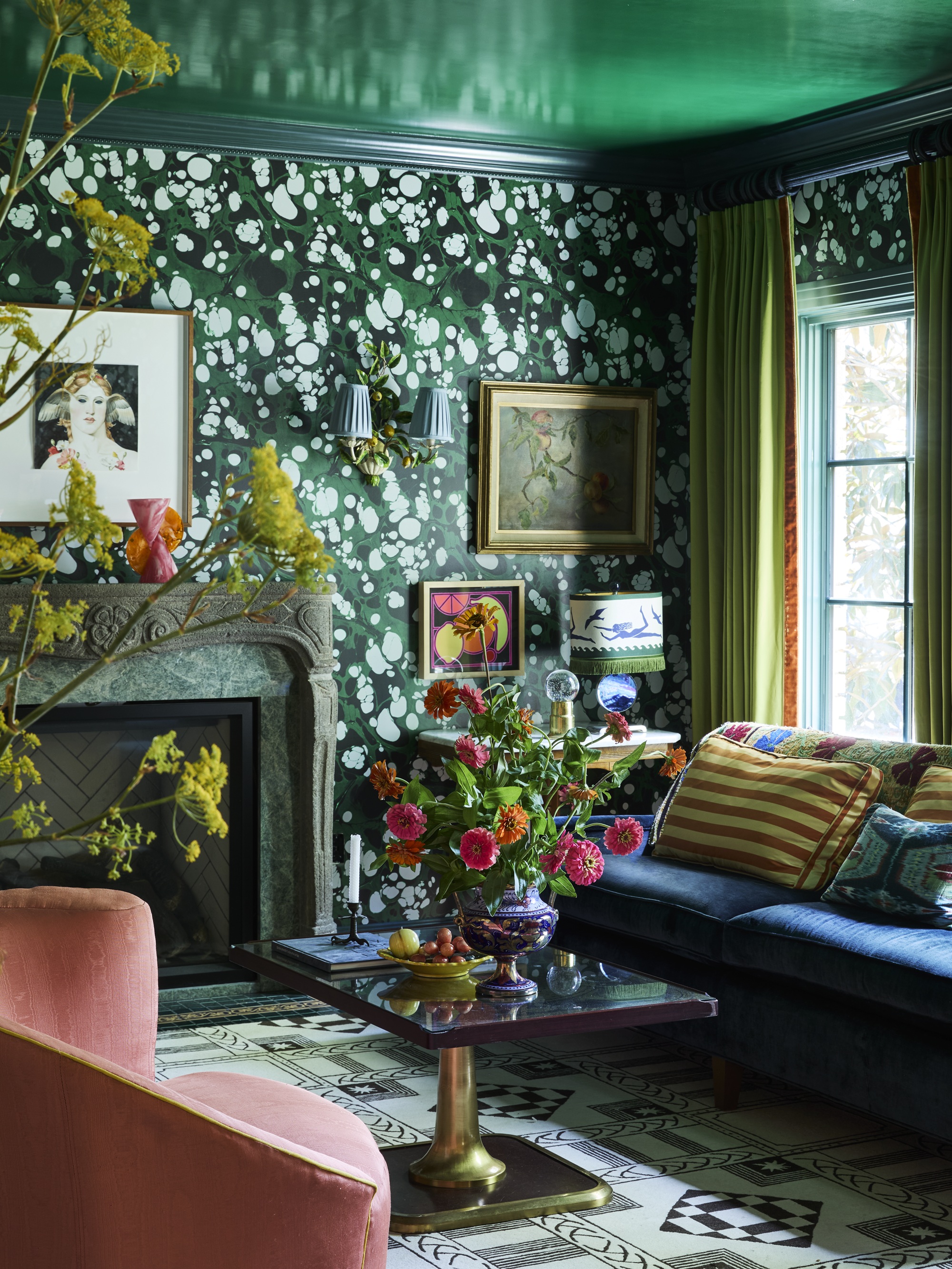 living room with green gloss ceiling, marbled wallpaper, ornate fireplace, blue sofa with striped cushion, pink armchair, black and gold coffee table with vase of flowers