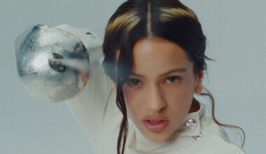 close-up photo of singer Rosalía with a halo-shaped highlight in her hair, pointing a sword into the camera
