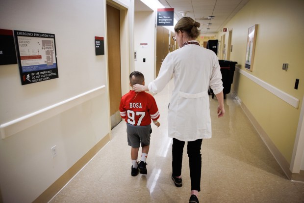 Patient Stephen De La Torre, 7, walks a hallway with Stanford Medicine radiation oncologist Dr. Susan Hiniker before receiving a proton cancer treatment at Stanford Medicine Cancer Center in Palo Alto, Calif., on June 10, 2026. (Dai Sugano/Bay Area News Group)