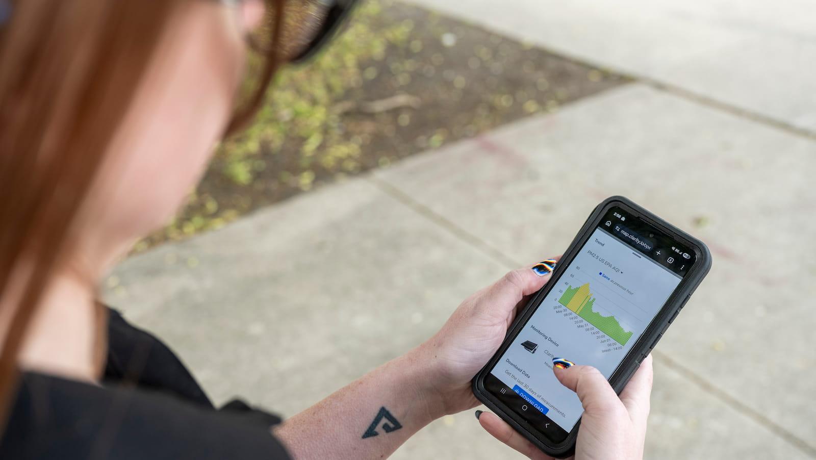 Woman holds phone looking up local air quality data.