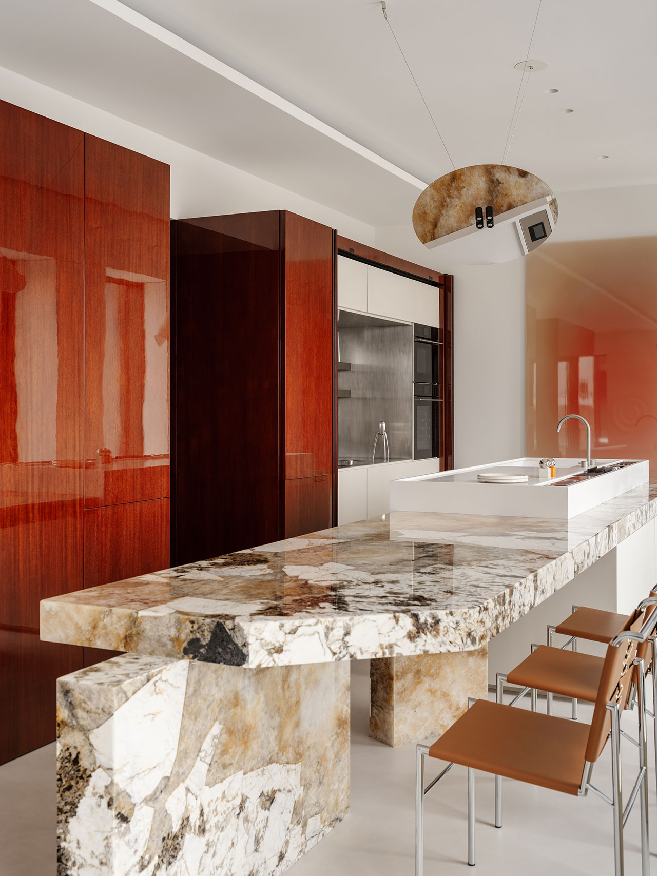 Modern Antwe kitchen with glossy reddish-brown cabinets, a marble island with bold veining, metal barstools with brown seats, and minimalist fixtures.