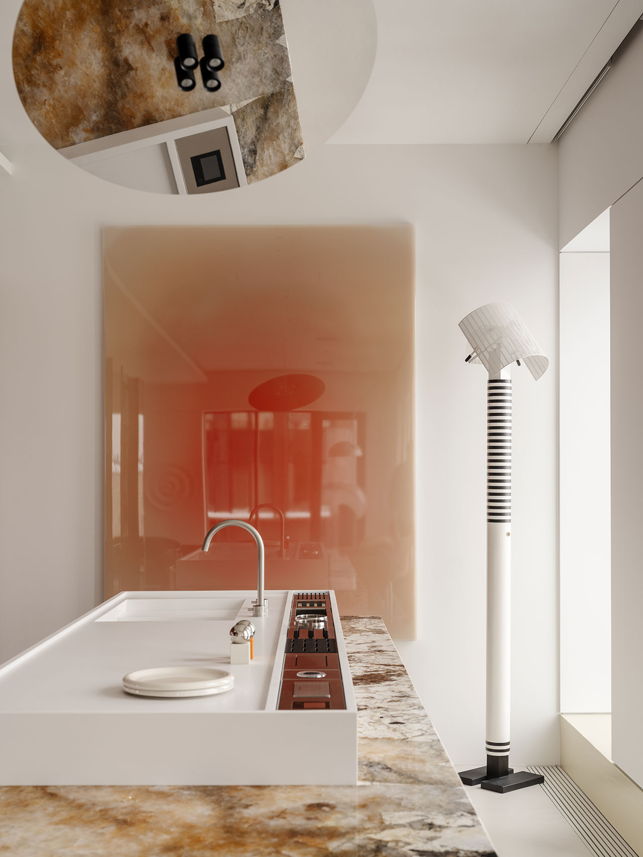 Modern kitchen with an Antwe marble countertop, integrated stove, minimalist white sink, striped floor lamp, and a large glossy red wall panel reflecting the room.