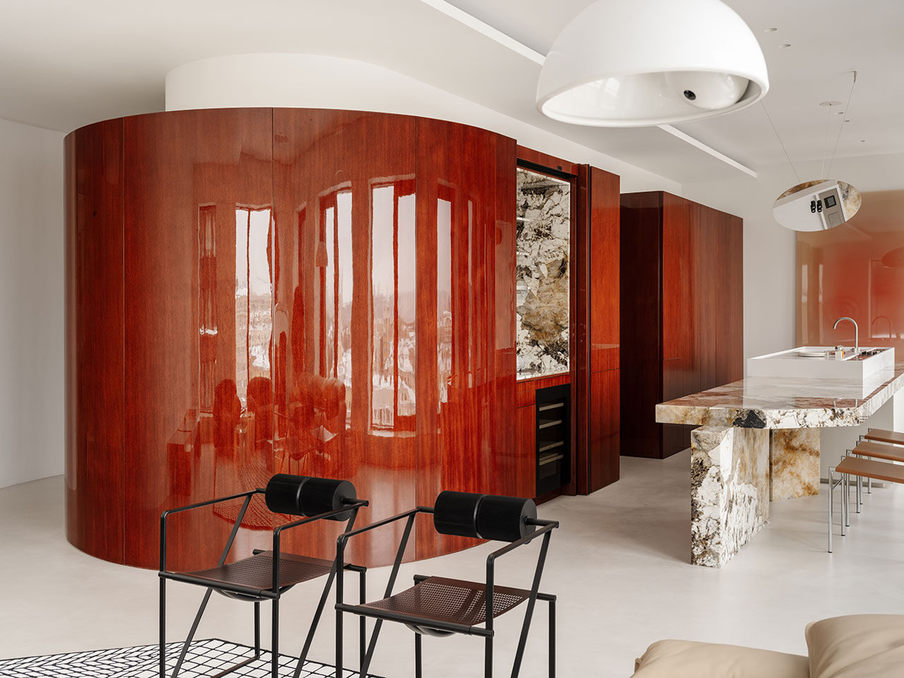Modern Antwe kitchen with curved, glossy wood cabinetry, a marble island, black metal chairs, and minimalist decor in a bright, open space.