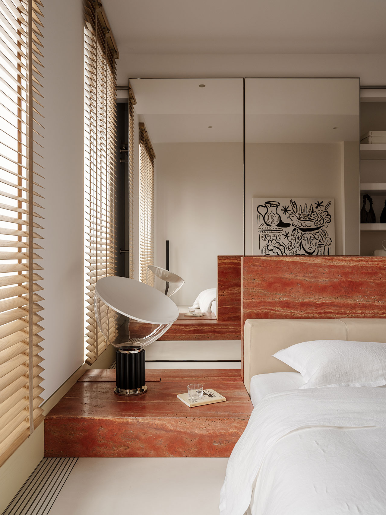 Modern Antwe bedroom with a large mirror, red stone headboard and nightstand, minimalist decor, a white lamp, and abstract art on the wall.