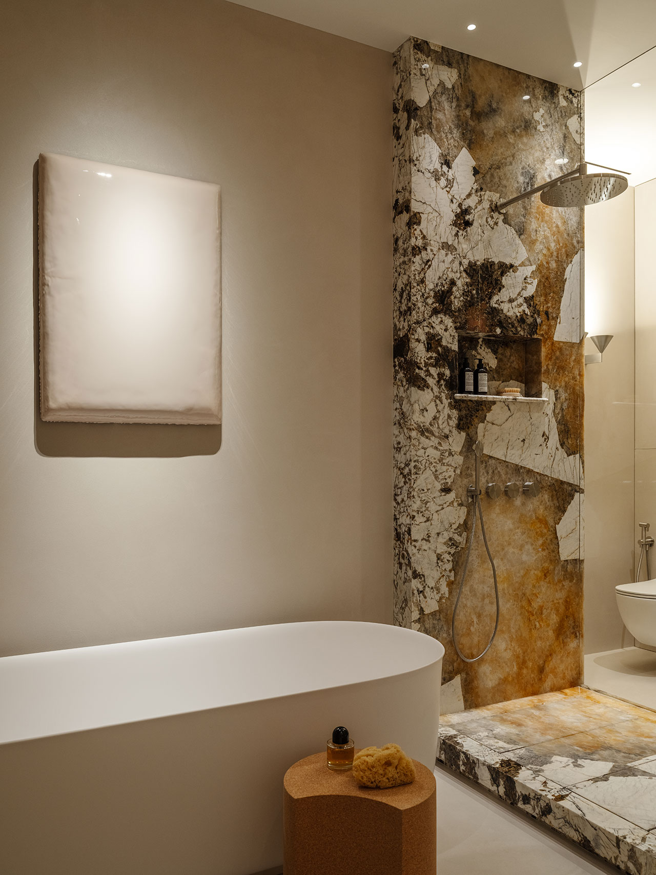 Modern Antwe bathroom with a freestanding white bathtub, marble shower area with rainfall showerhead, wall art, and a small round side table holding bath items.