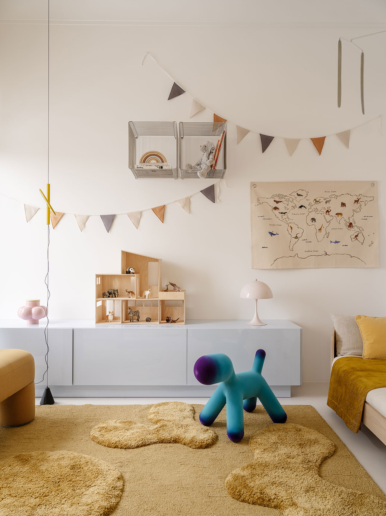 Modern children's room with yellow and beige decor, Antwe geometric rug, wall bunting, toy storage, a blue-green dog-shaped seat, and a world map wall hanging.