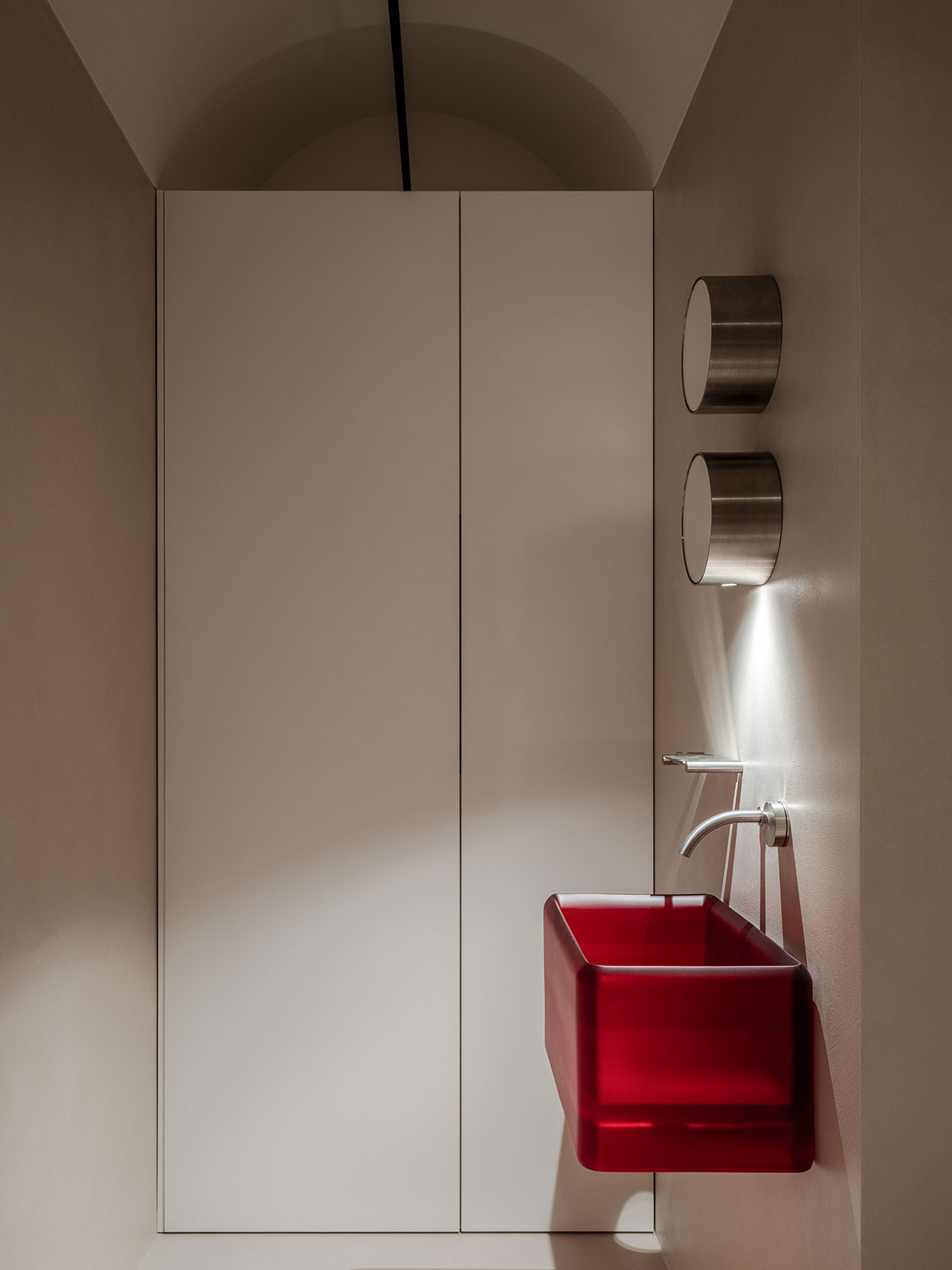 Minimalist bathroom with a striking Antwe red rectangular sink, wall-mounted faucet, two cylindrical stainless steel containers, and plain light-colored walls and doors.