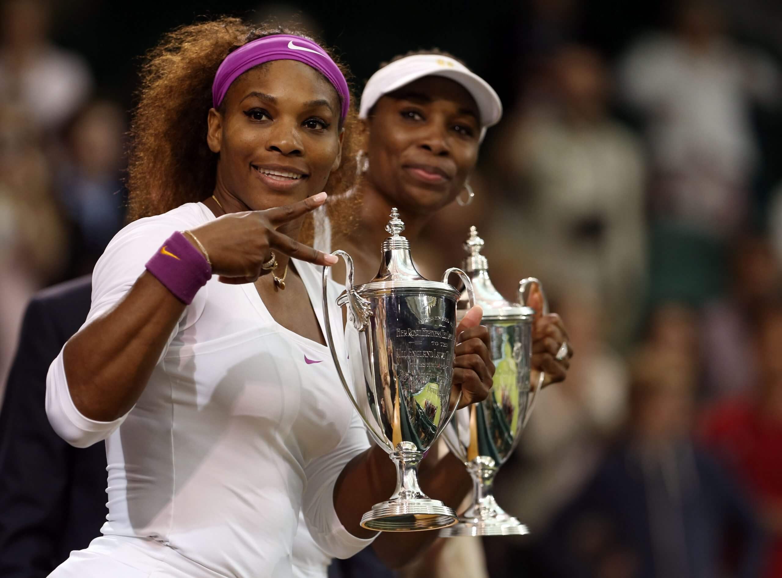 Serena Williams poses holding a Wimbledon trophy alongside her sister, Venus.