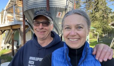 A man and a woman sit in front of a large grey metal water tank on their property.