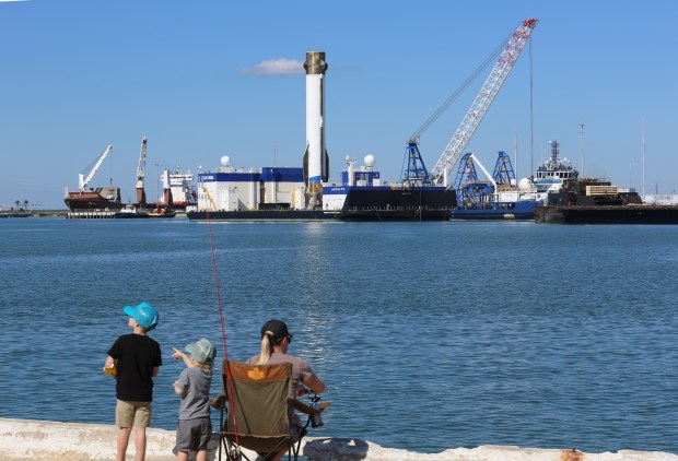 Jennifer Kretschmer and her children Landen, 2, and Bryce, 7, of Rockledge, try their hand at fishing while watching the Blue Origin New Glenn rocket's first-stage booster "Never Tell Me The Odds" after it arrived to Port Canaveral on Tuesday, Nov. 18, 2025. Jeff Bezos' company joins SpaceX as one of two that have successfully recovered orbital-class boosters as part of their goals to reduce launch costs. The New Glenn booster is designed for as many as 25 launches. Its recovery was the first having landed on the recovery ship Jacklyn, named after Bezos' mother, on then NG-2 mission about 375 miles out in the Atlantic, before making the trip back to port. (Richard Tribou/Orlando Sentinel)
