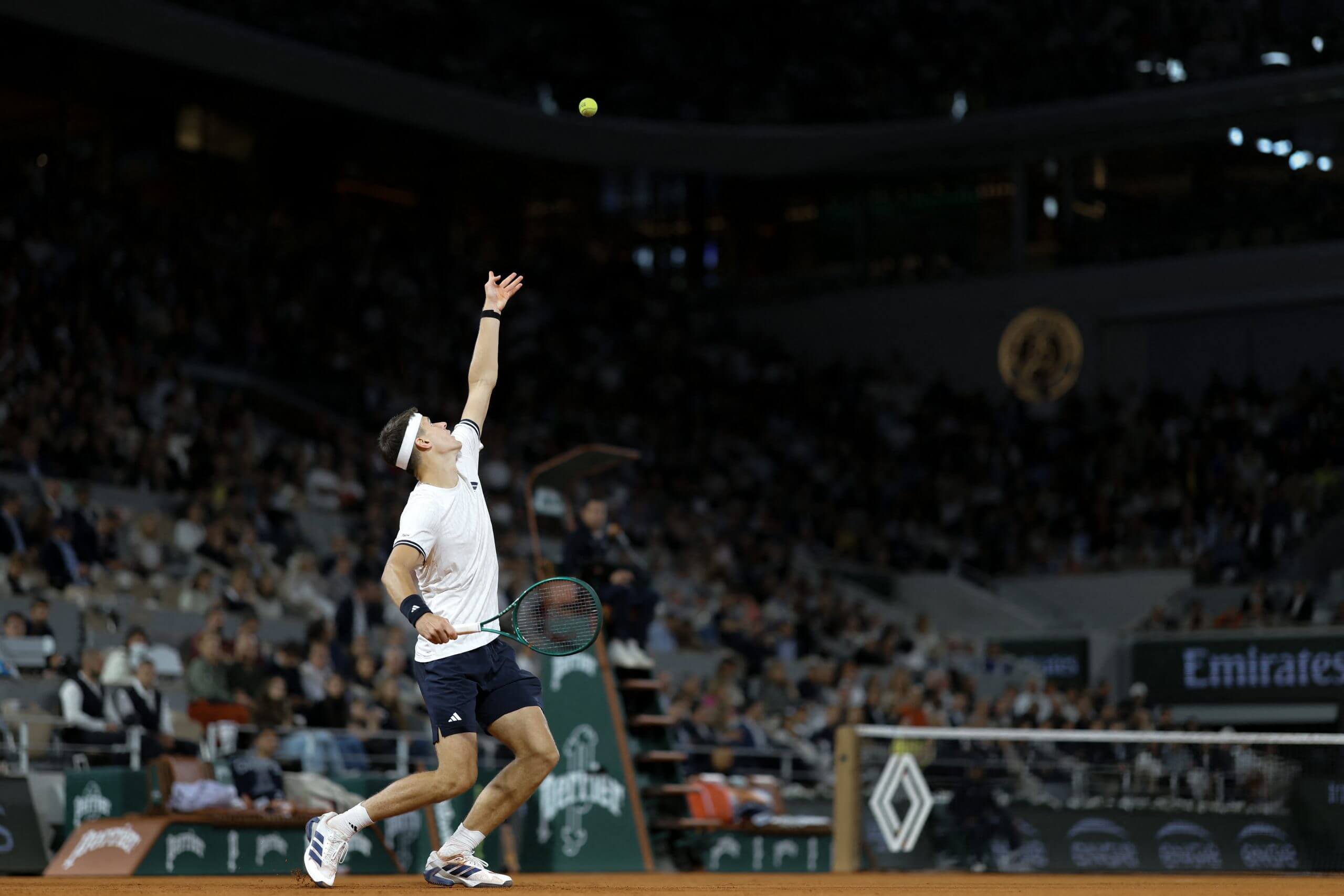 Jakub Menšík tosses a tennis ball in the air to hit a serve.