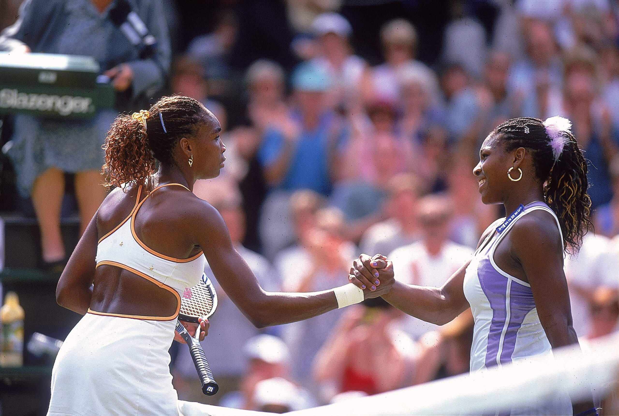 Venus Williams (left) and Serena Williams (right) shake hands over the top of a tennis net.