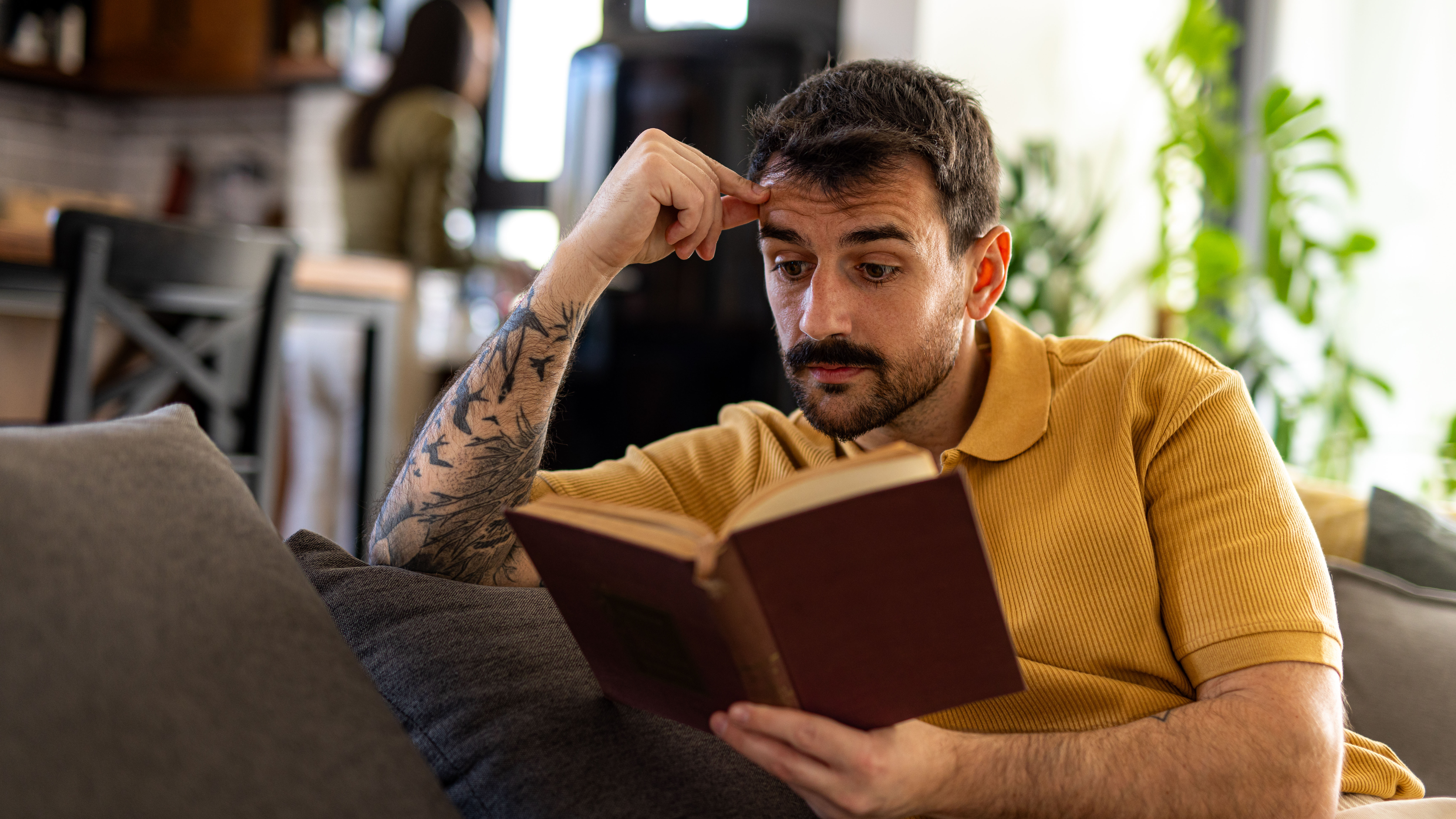 Young man concentrating while reading a book, sitting on a sofa.