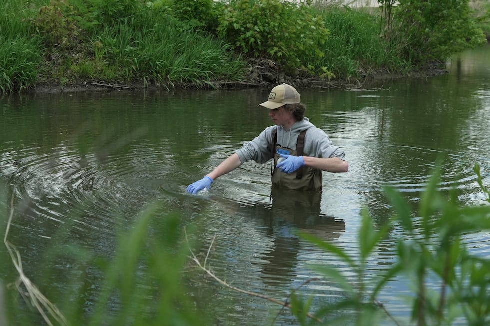 Drake University student Harrison Ziegler dips a bottle in a stream to collect a water sample...