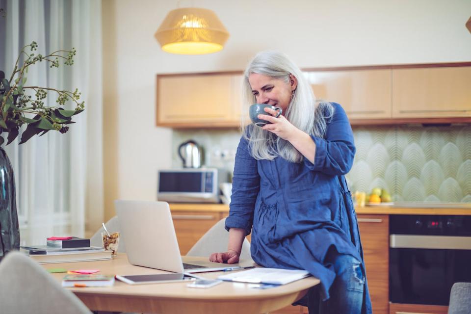 Smiling person drinking from mug and looking at laptop.