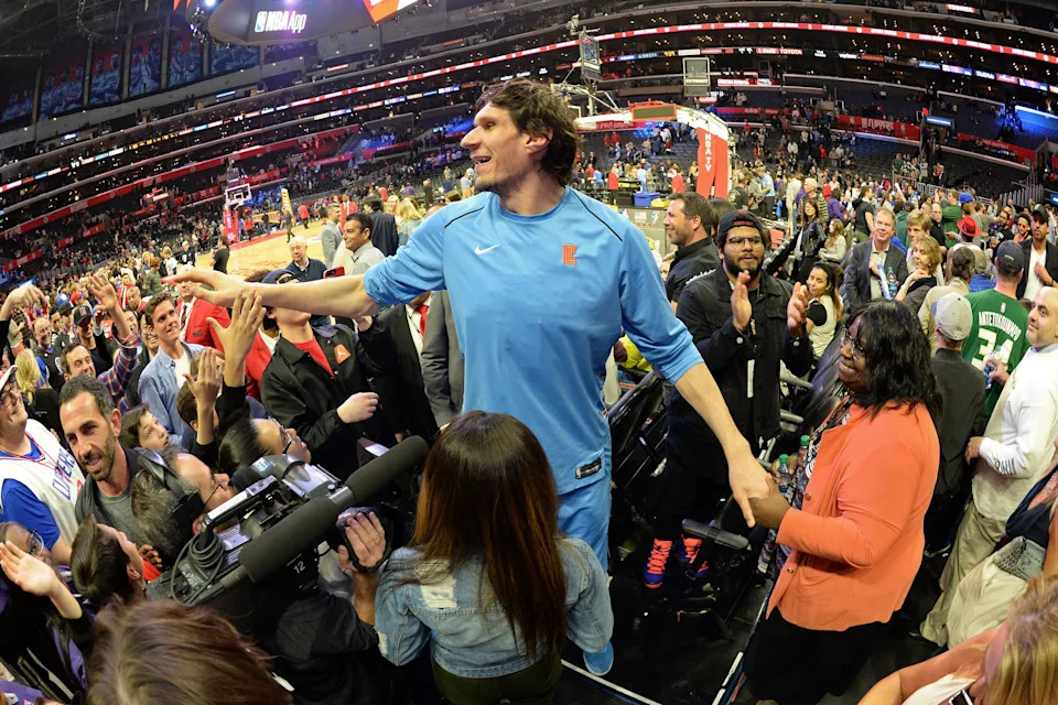 Basketball player in team tracksuit interacts with fans courtside at a crowded arena