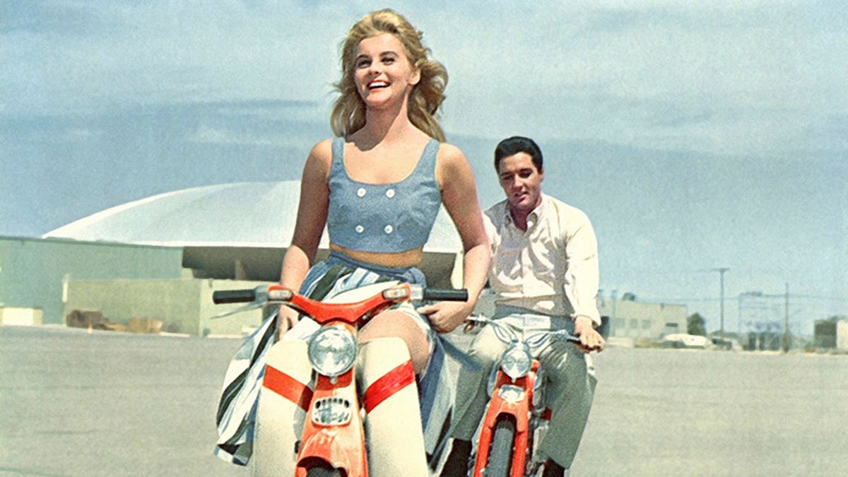 Ann-Margret and Elvis Presley riding motor scooters in a film scene.
