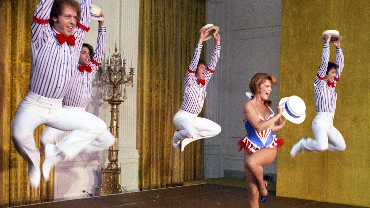 Ann-Margret performing with male backup dancers mid-air in striped shirts and bow ties